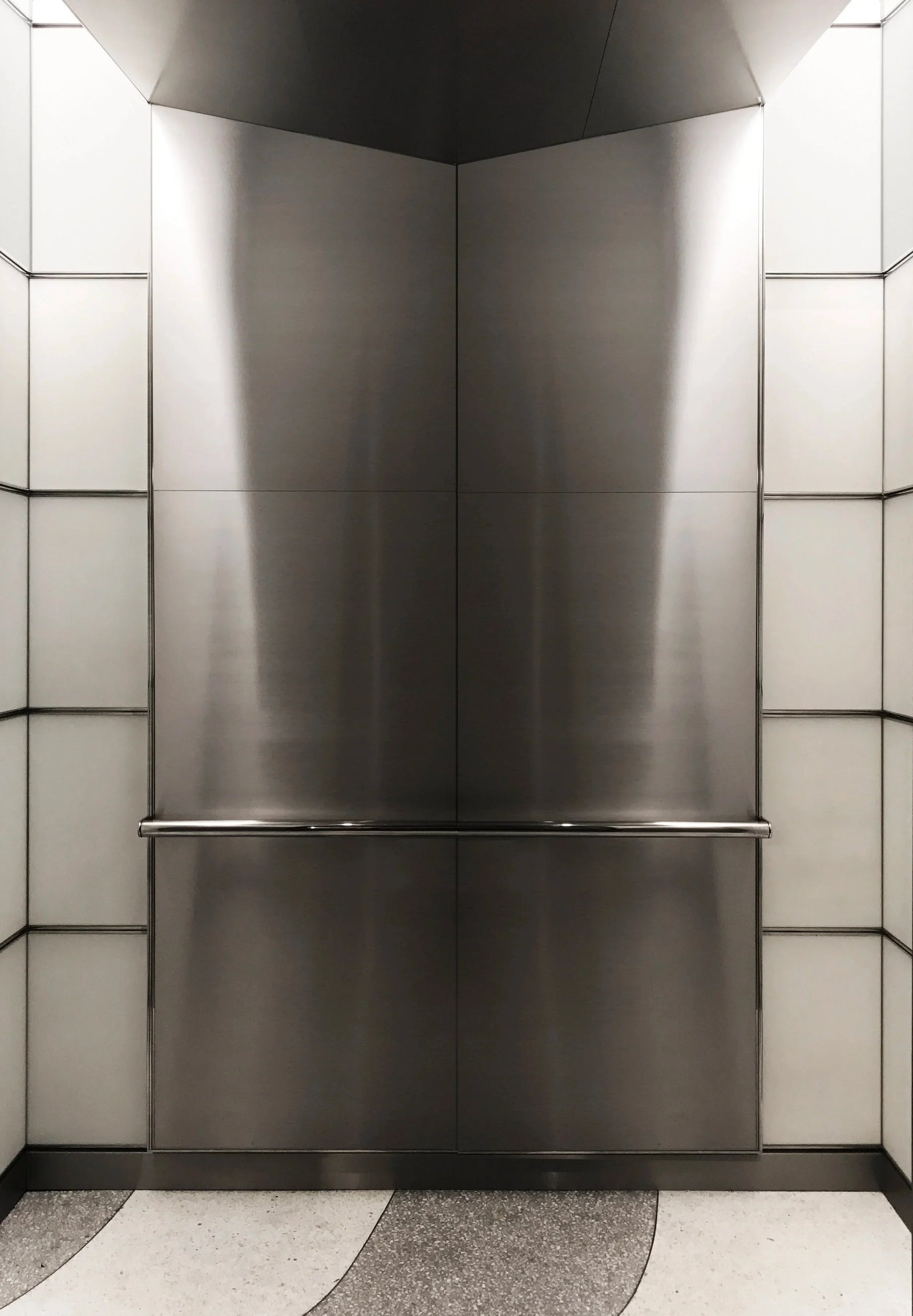 Stainless steel elevator interior with brushed wall panels and a continuous handrail