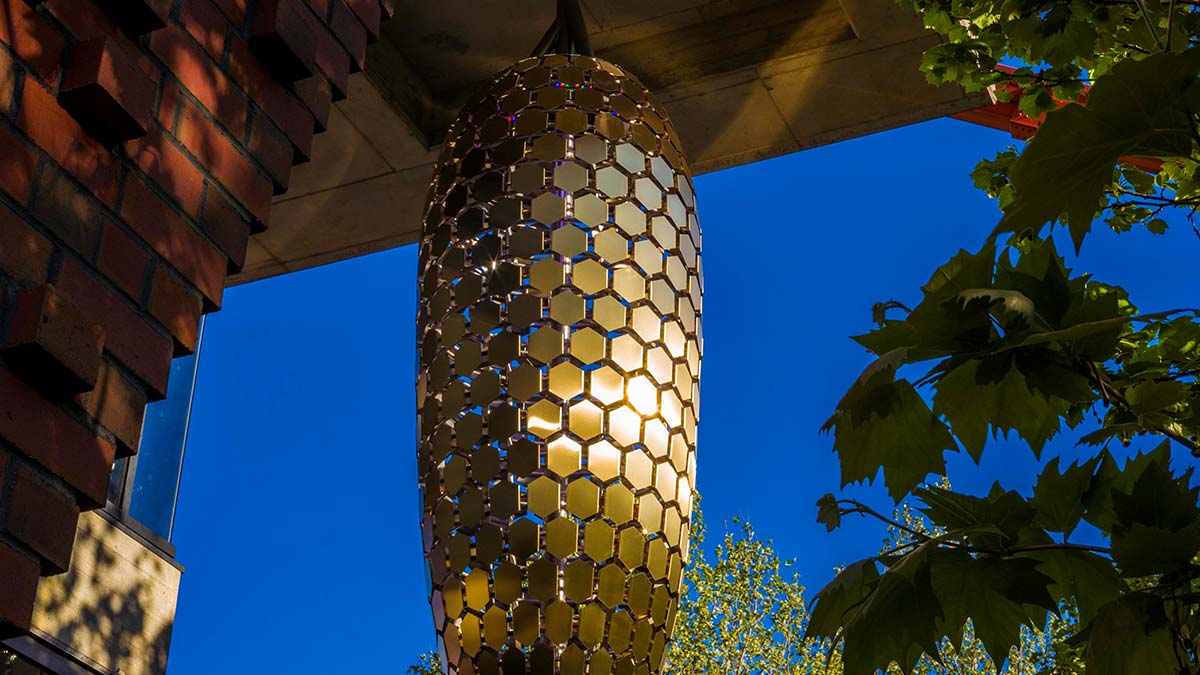 Gold satin stainless steel beehive artwork at Curtin University, photographed at dusk