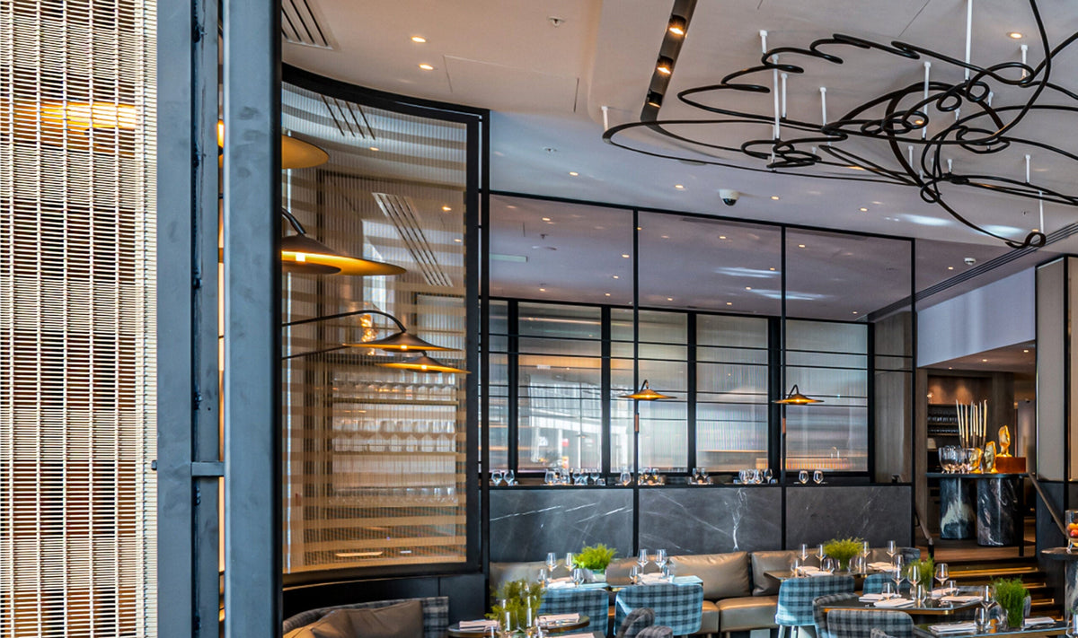 Curved framed woven-metal room divider panels defining a restaurant dining area at The Londoner Hotel