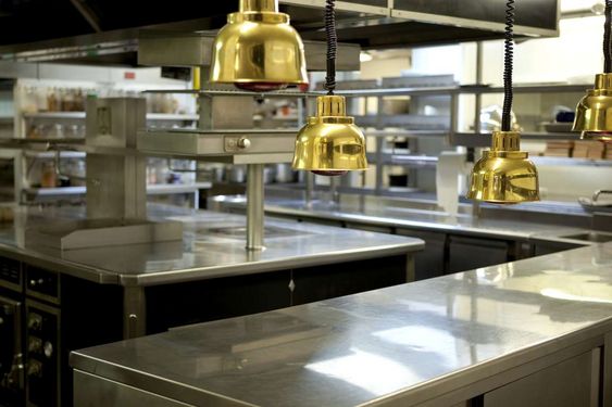 Stainless steel food-service counters beneath heat lamps in a professional kitchen