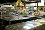 Stainless steel food-service counters beneath heat lamps in a professional kitchen