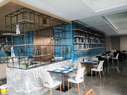 A stainless steel hotel bar counter and wine display shelving serve the Hilton lobby and dining area.