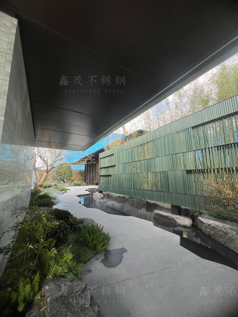 Dark stainless steel ceiling panels line the covered approach beside a landscaped water feature at Suzhou Longfor Shanghe Song Sales Gallery.