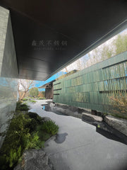 Dark stainless steel ceiling panels line the covered approach beside a landscaped water feature at Suzhou Longfor Shanghe Song Sales Gallery.