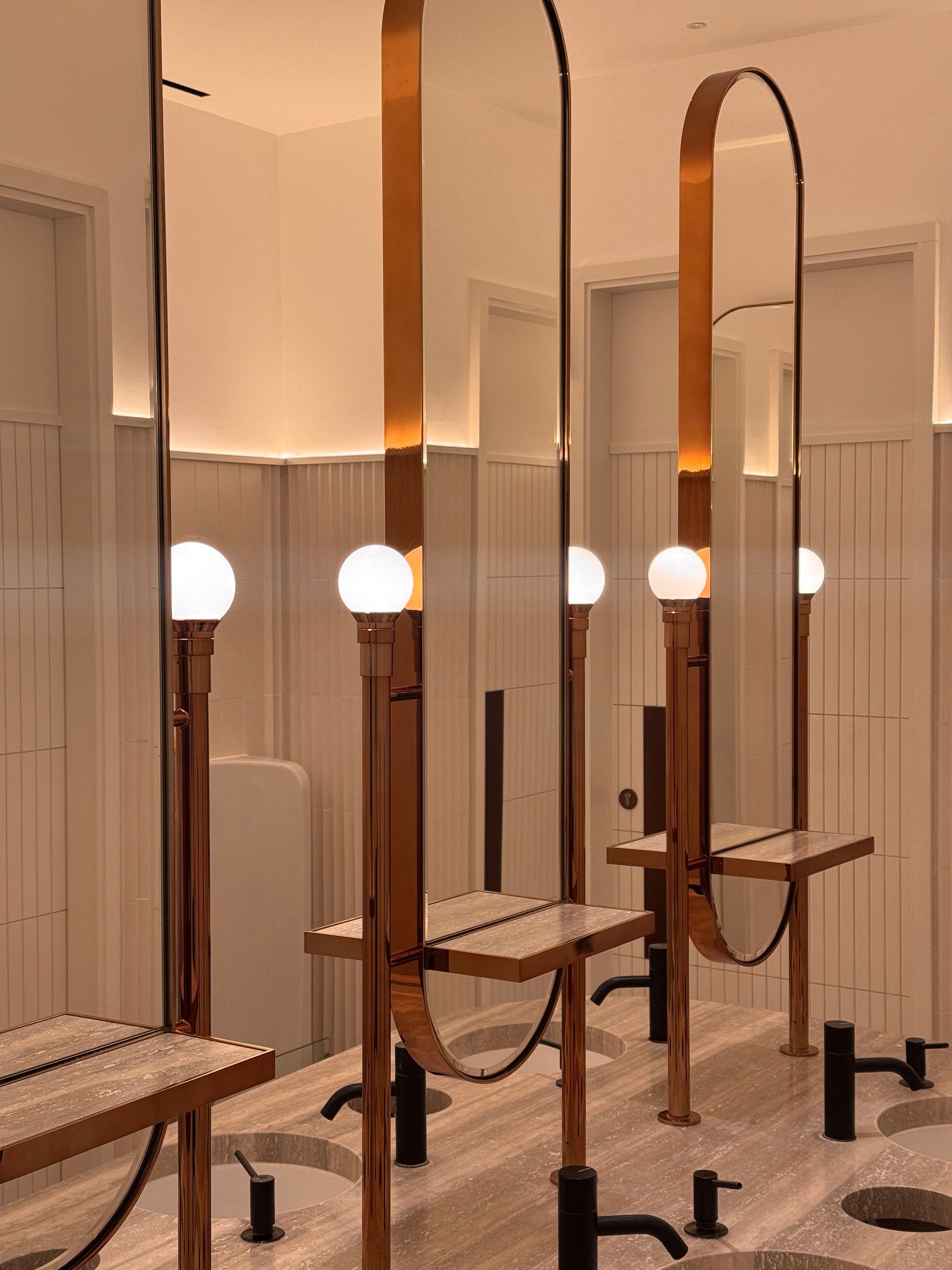 Tall bronze mirror cabinets with shelf details at a vanity