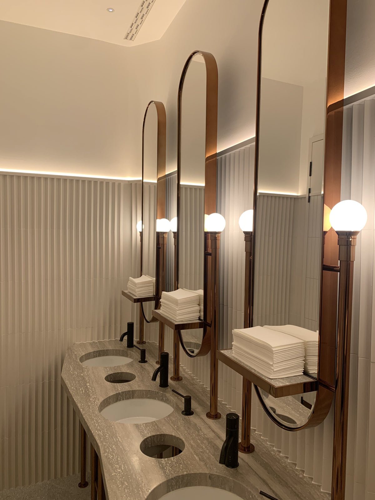 Rounded bronze mirror cabinets with shelf detail at a vanity