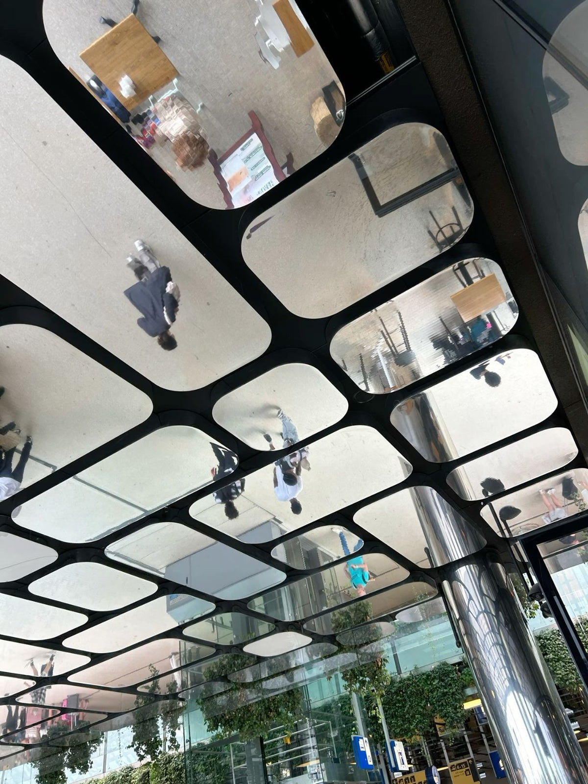 Upward view of rounded mirror ceiling modules reflecting people below