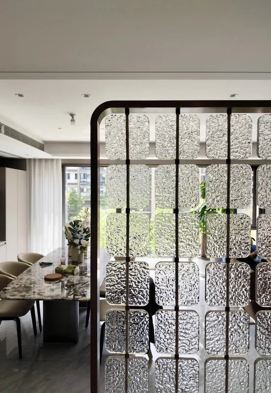 Black-framed stainless steel screen with textured glass panels beside a dining area