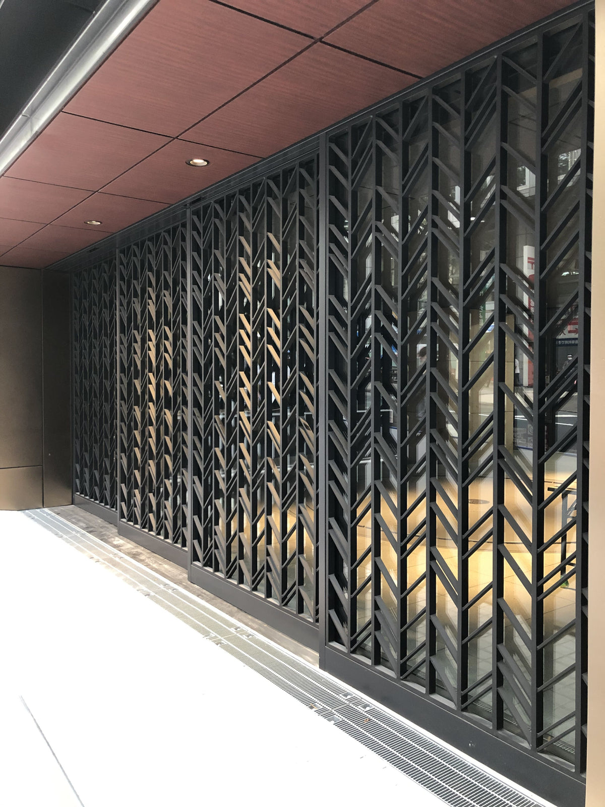 Black stainless steel screen wall with a repeating chevron pattern in an interior corridor.