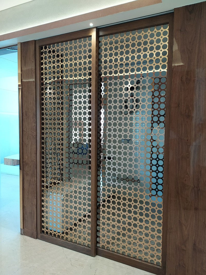 Bronze-toned stainless steel screen panels with repeating circular openings at an interior entrance.