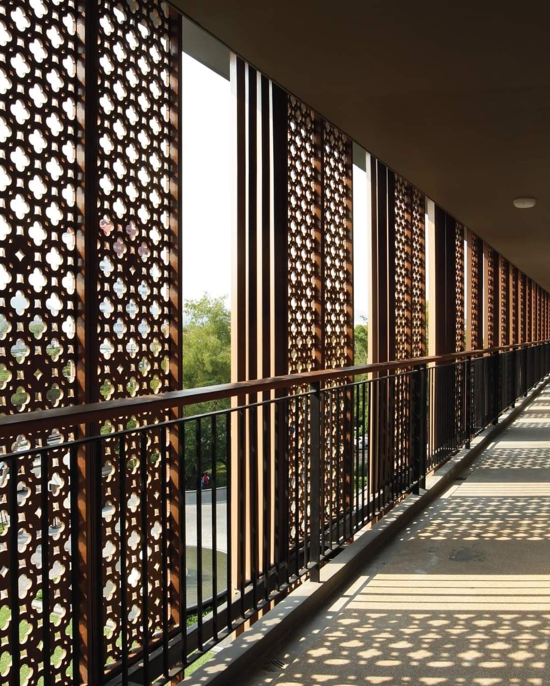 Dark decorative stainless steel screen panels with repeating floral cut-outs along an elevated walkway.