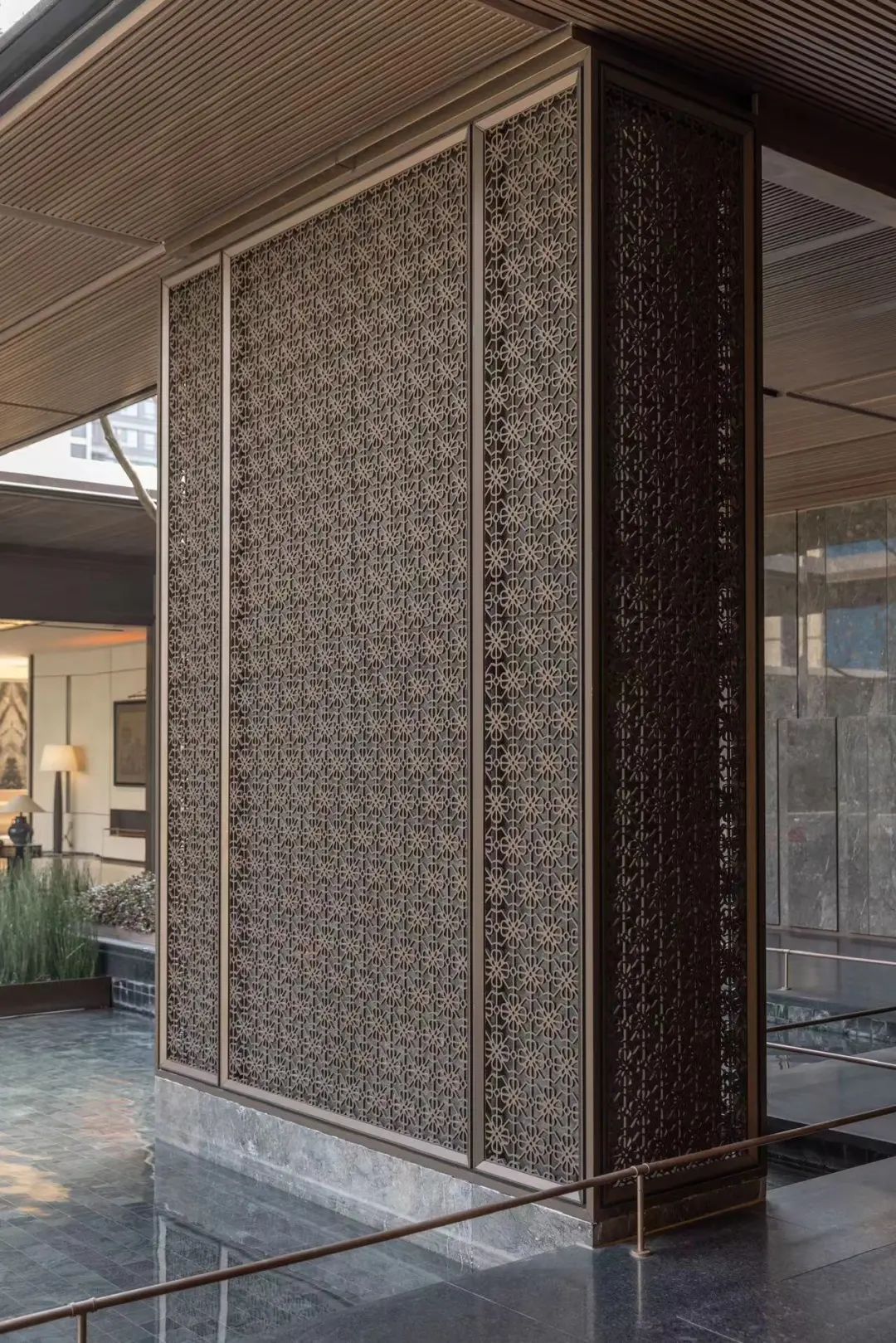 Framed stainless steel screen panels with a fine geometric cut-out pattern dividing an architectural interior.