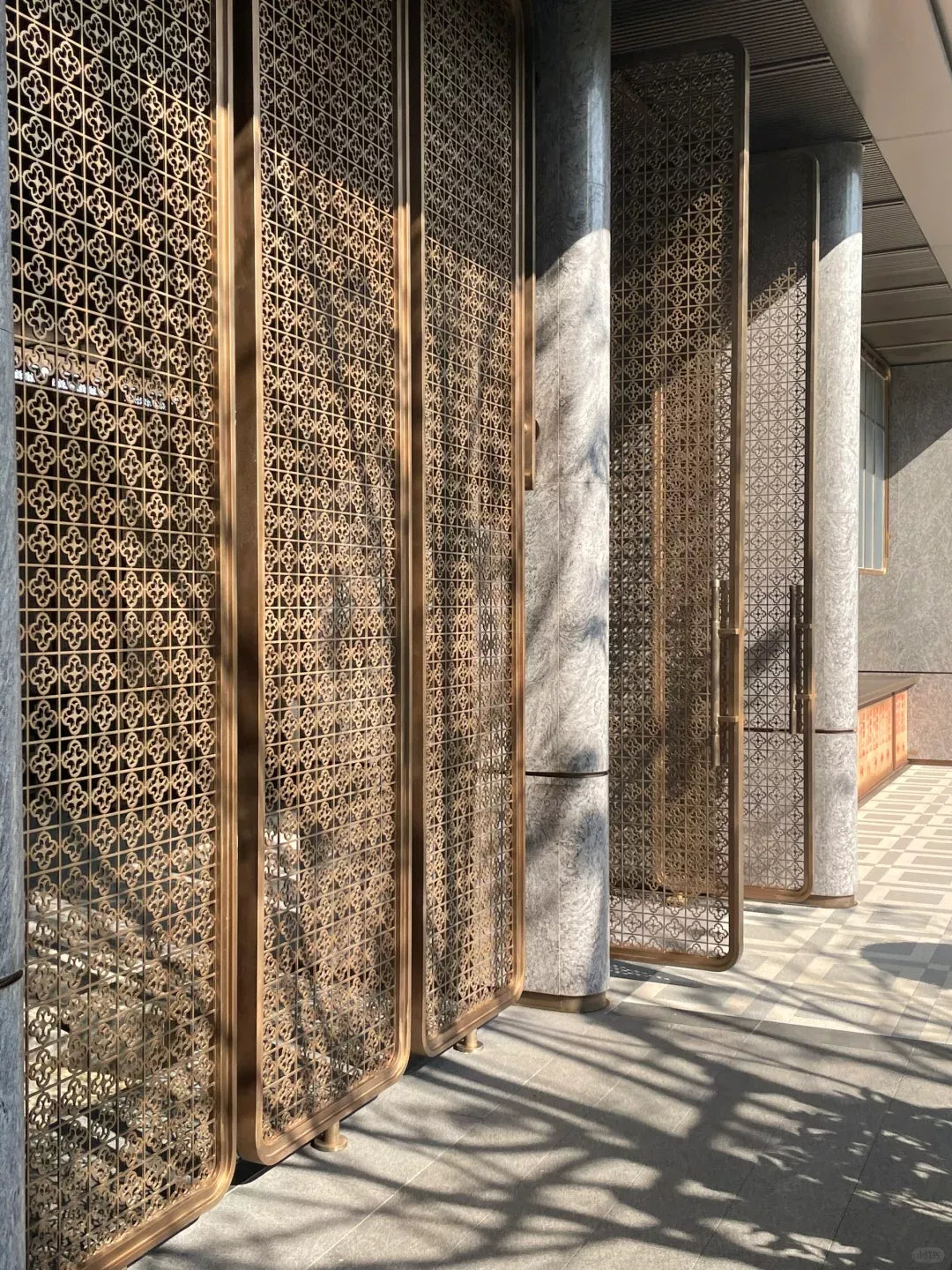 Bronze-toned framed stainless steel room divider panels with repeating quatrefoil cut-outs along an entrance.