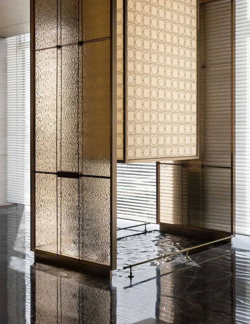Bronze-toned stainless steel framed screen with textured translucent panels in a lobby interior.