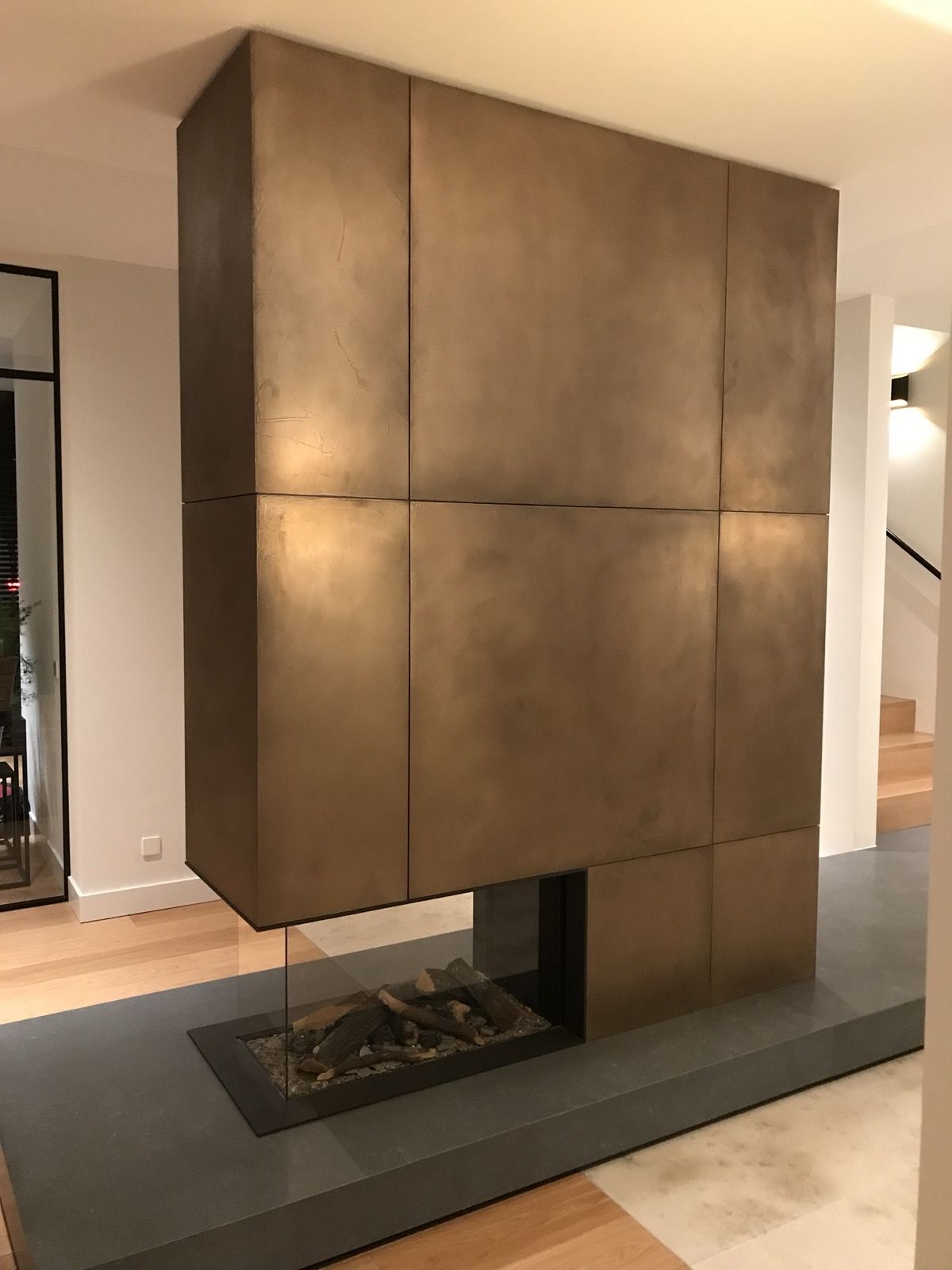 Bronze-toned textured stainless steel wall panels surrounding a fireplace.