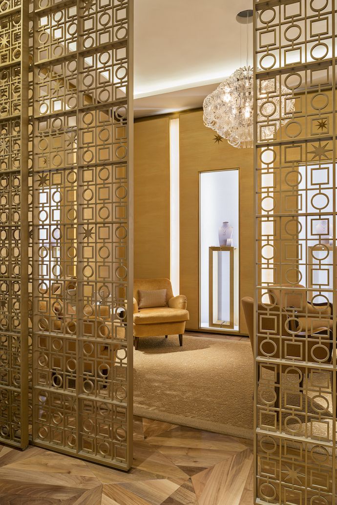 Gold-toned stainless steel screen panels with mixed geometric circles, squares and star motifs at an interior entrance.
