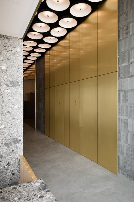 Gold-toned stainless steel wall panels lining a corridor beneath circular ceiling lights.