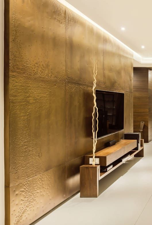 Gold-toned textured stainless steel wall panels with a television niche in a living room.