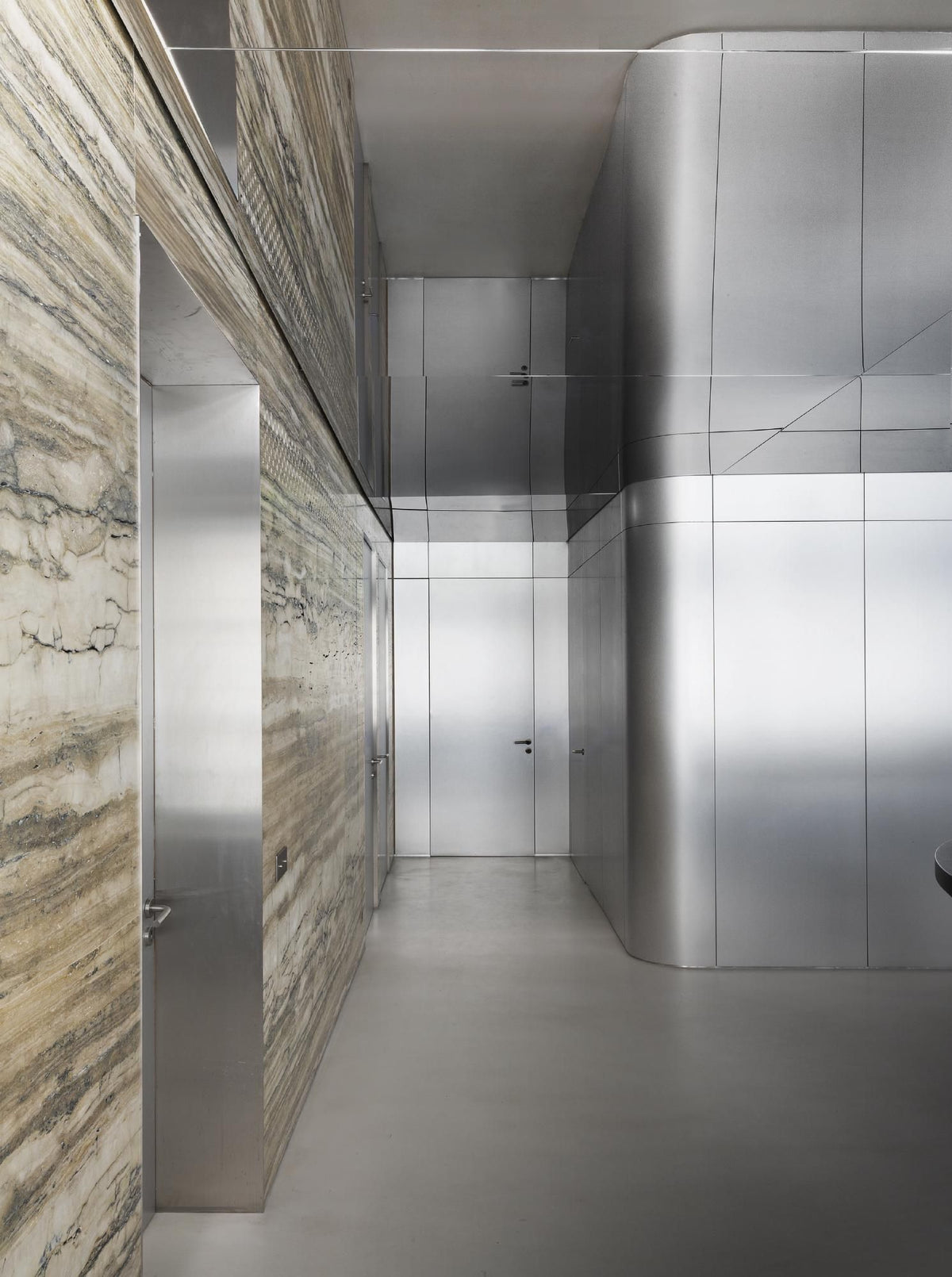 Silver stainless steel wall cladding with curved sections in a modern corridor.