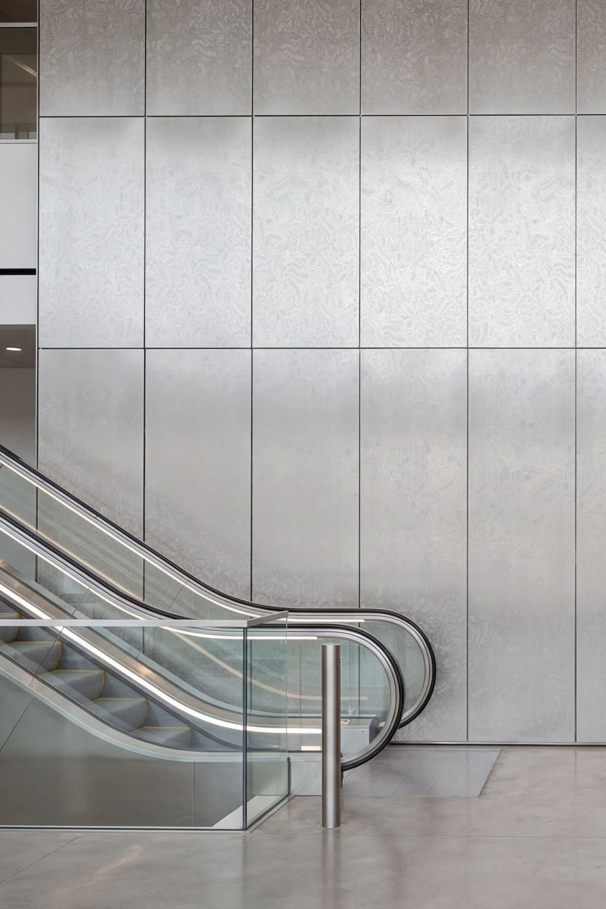 Silver textured stainless steel wall panels beside an escalator in a commercial interior.
