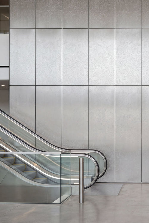 Silver textured stainless steel wall panels beside an escalator in a commercial interior.